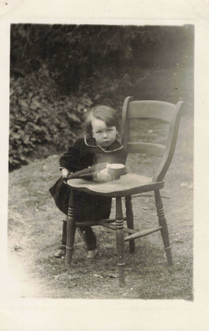 Old real photo postcard of a child with a chair in the garden